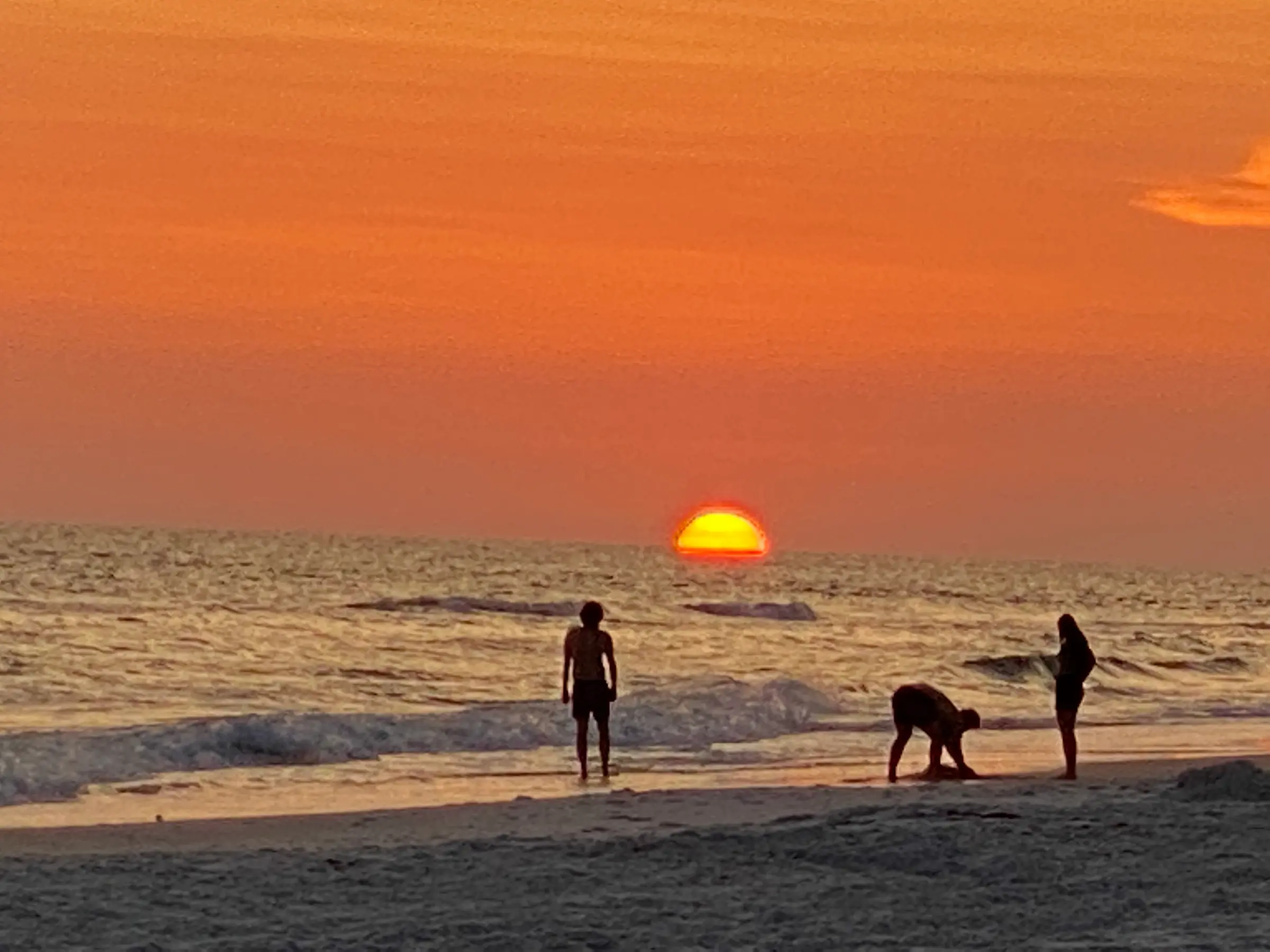 Sunset beach scene with silhouetted people.