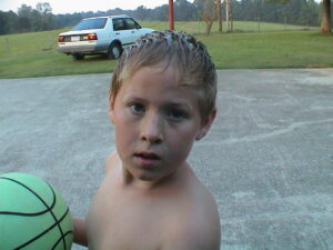 Boy holding basketball outdoors near parked car.