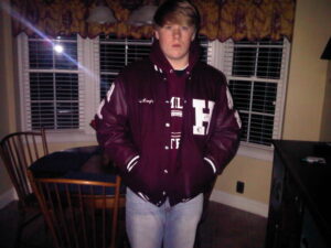 Person in varsity jacket standing indoors at night.