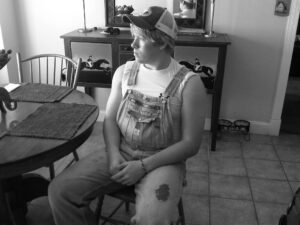 Person in overalls sitting at kitchen table.
