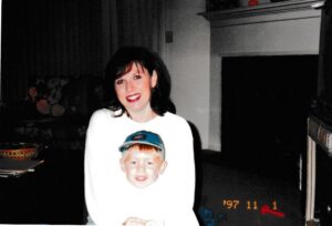 Woman and child smiling indoors by fireplace.